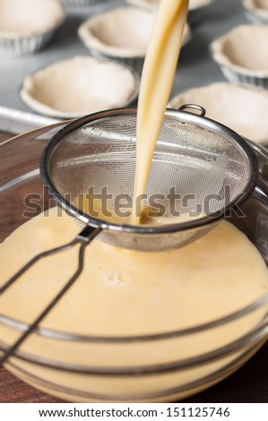 Pouring the mixture through a sieve into a glass bowl for smooth mixture egg custard cream.