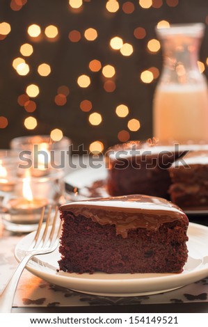 Still life of chocolate cake and a bottle of milk with blurry christmas lights.