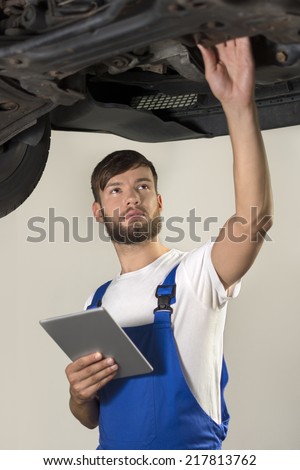 Male car mechanic working under car with tablet PC, Studio Shot