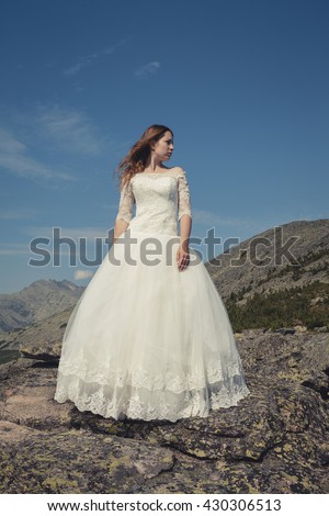 bride in wedding dress in the mountains is in the wind and looks into the distance