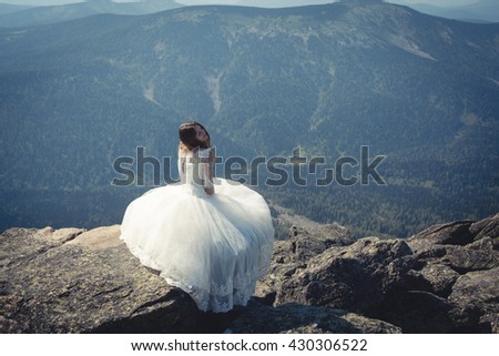 bride in wedding dress sitting on a rock over a precipice