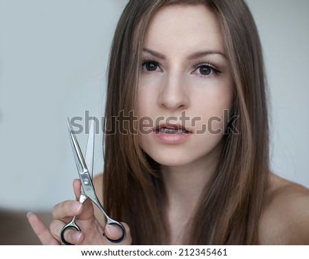 Female model posing with scissors on a white background with a strong look, closeup