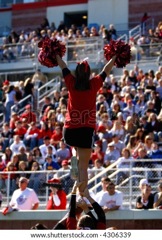 A football cheerleader is raised into the air in front of a large collegiate crowd.