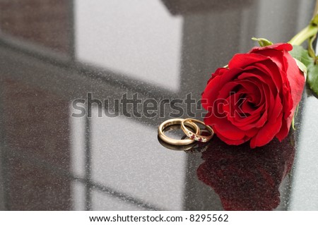 A couple's wedding bands next to a red rose.