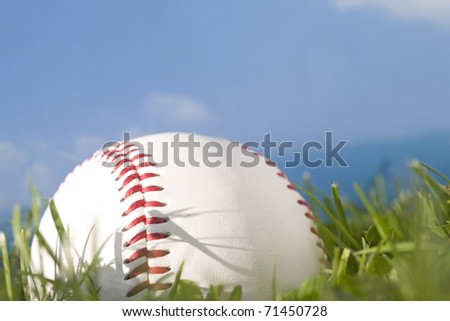 Summer baseball concept with a baseball in the outfield grass against a perfect blue sky.