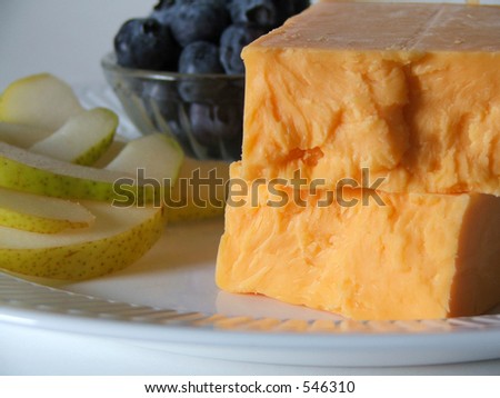 Block of cheese in foreground, with fresh fruits in the background.