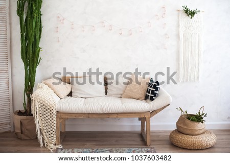 Beautiful spring decorated interior in white textured colors. Living room, beige sofa with a rug and a large cactus.