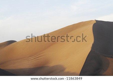people hiking walking and climbing up on sand dune desert in sunset