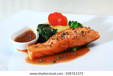 Grilled  Salmon Steak with vegetables,pepper seeds. and sauce on a white plate.