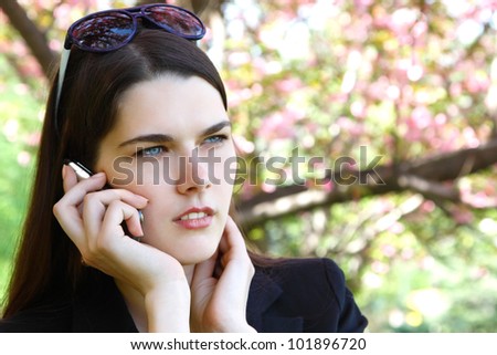 beautiful troubled girl calling phone over blooming spring garden