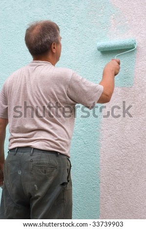 man painting wall with a roll in green outdoor