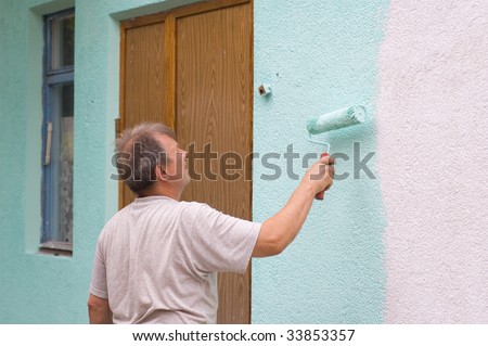 man painting wall with a roll in green outdoor