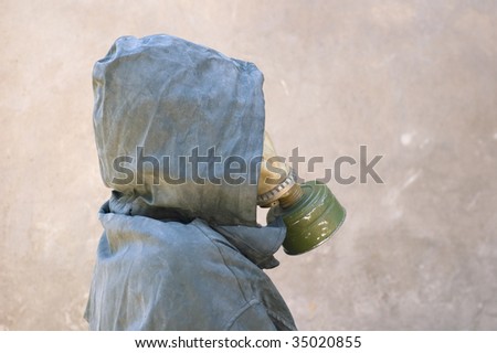 man in gas mask and dirty waterproof cape-tent with hood against cement wall