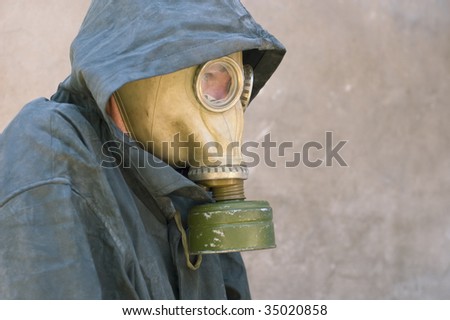 man in gas mask and dirty waterproof cape-tent with hood against cement wall