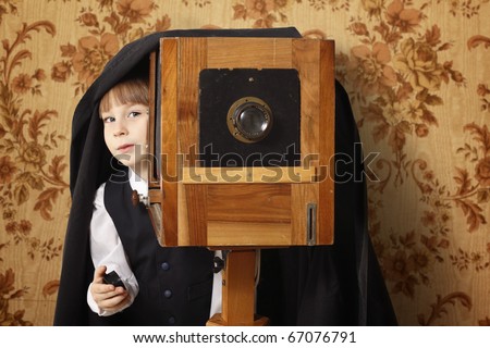cheerful boy retro photographer with vintage camera over old wallpaper background