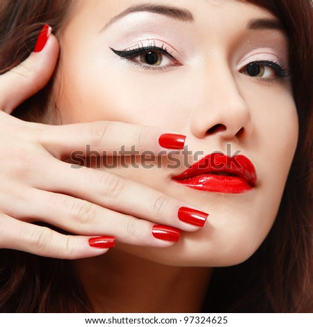 beautiful young female face with vivid red lipstick and nail polish closeup