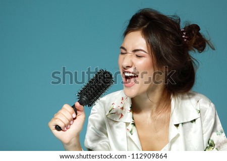 Cheerful attractive teen girl sing song holding comb like a microphone in the morning. Over blue background.
