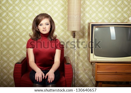 art portrait of young woman sitting on chair and looking at camera in room with vintage wallpaper and interior, retro stylization 60-70s, toned
