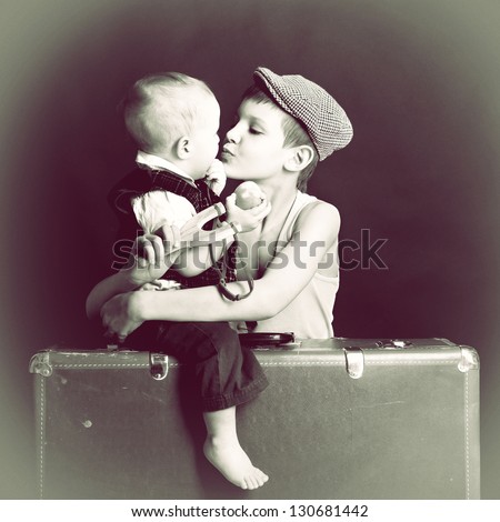 vintage art portrait of little boy hugs and kiss his baby brother leaning on old suitcase, retro stylization of 30-50s, toned