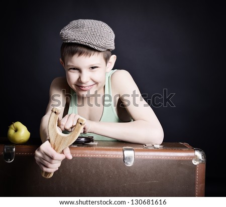 vintage art portrait of little boy looking at camera holding catapult and  leaning on old suitcase, retro stylization of 30-50s