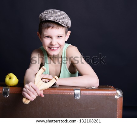 vintage art portrait of little boy looking at camera holding catapult and  leaning on old suitcase, retro stylization of 30-50s