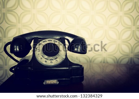 vintage old telephone, black retro phone is on wooden table over green old-fashioned wallpaper