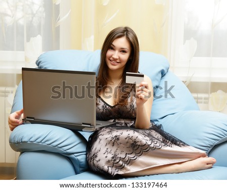 Happy young woman shopping online with credit card and computer sitting on sofa at home. Internet shopping