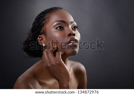 Beautiful young african woman posing at studio, face with hand portrait over dark background