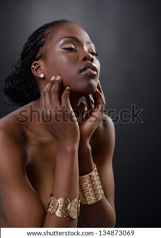Beautiful Young African Woman Posing At Studio In Golden Jewellery, Face With Hand Portrait Over Dark Background