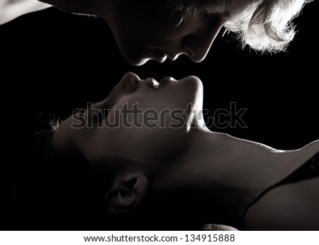 Sexy passion couple, beautiful young man give woman kiss in love, faces closeup in profile. Silhouette, toned, studio shot over black