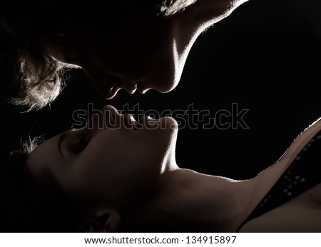 Sexy passion couple, beautiful young man give woman kiss in love, faces closeup in profile. Silhouette, toned, studio shot over black