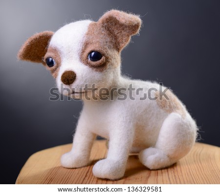 Toy dog, hand made puppy sitting in studio on wooden stool, felting