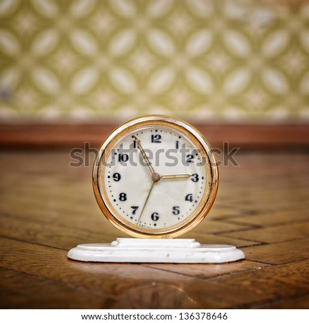 Retro clock on the weathered wooden parquet floor in vintage room with old fashioned wallpaper