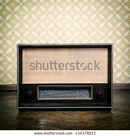 vintage radio receiver device on the weathered wooden parquet floor in vintage room with old fashioned wallpaper, toned