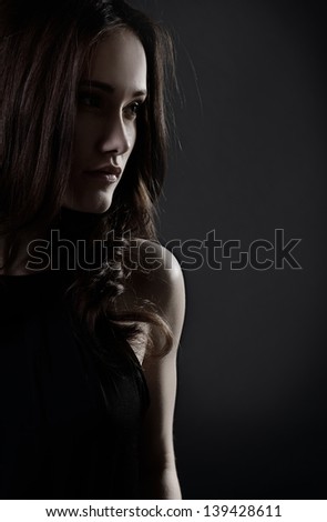 Young woman with beautiful long brown hair posing at studio, profile over black background, toned