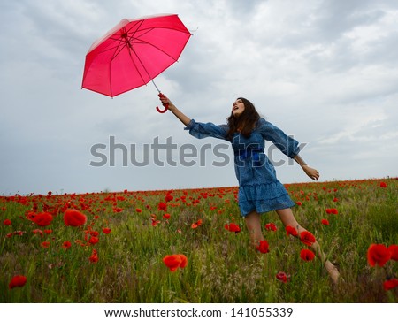Young beautiful woman flying with wind holding red umbrella from a poppy field, summer outdoor.