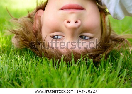Happy little boy standing upside down on green grass in spring park