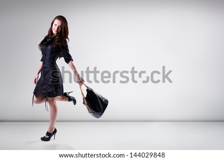 Beautiful young woman in black dress with bag posing at studio, full length portrait