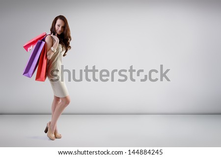 Beautiful young fashion woman posing at studio with shopping bags, full length portrait