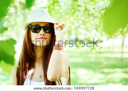 fashion girl outdoor portrait, young woman walking in summer park  in sunglasses and fedora with long brown hair, toned and noise added