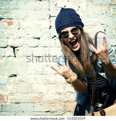 Portrait Of Beautiful Cool Girl Gesturing In Hat And Sunglasses Over Grunge Wall