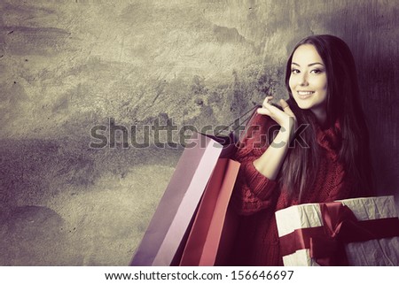beautiful young woman holding colored shopping bags and gift box over grunge concrete wall, holiday seasonal concept, toned