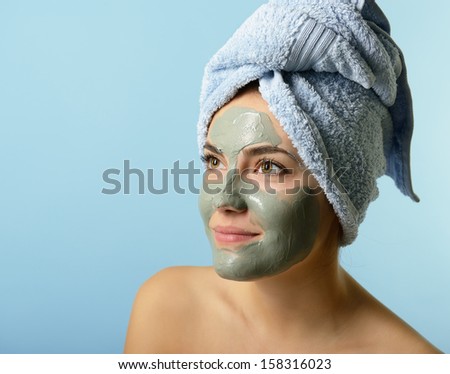 Beautiful young woman with clay facial mask, beauty treatment over blue