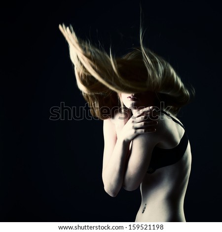 Fashion girl. Young beautiful woman with long blond hair fly-away over black background, toned