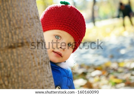 Little Red Riding Hood with grey wolf on background. Cute playful little girl  look out of tree in autumn park. Portrait of adorable child has fun fall outdoor.