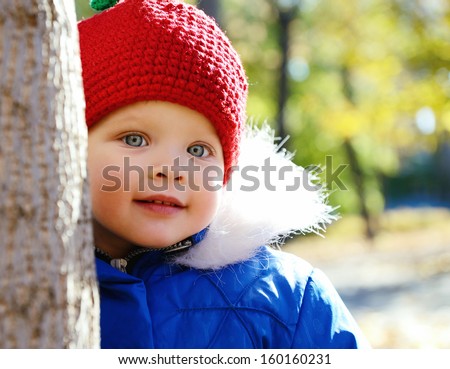 Cute playful little girl  look out of tree in autumn park. Portrait of adorable child has fun fall outdoor.