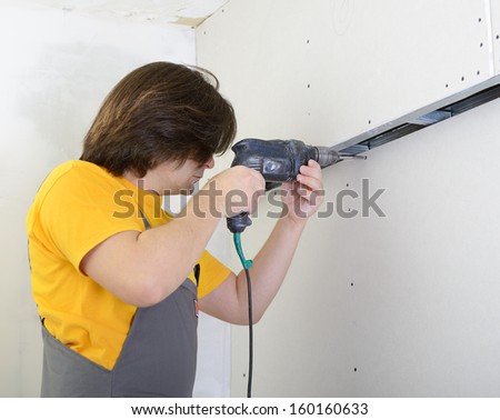 Man using drill to attach drywall panel to wall