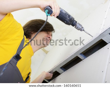 Man using drill to attach drywall panel to wall. Work with plasterboard
