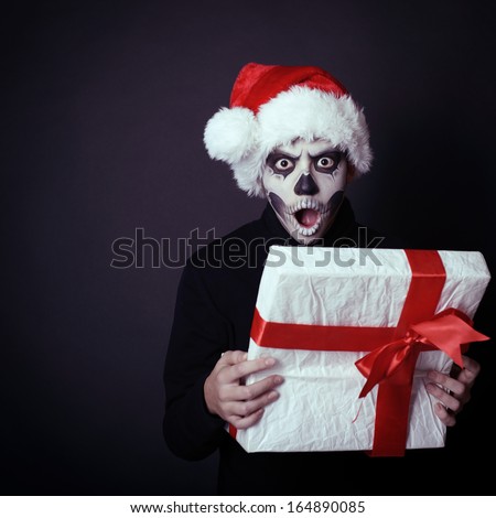 Holiday background of halloween person with terrible skull make-up in santa\'s hat opening gift box, toned
