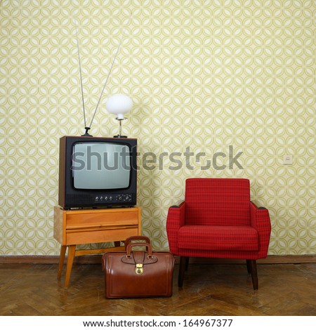 Vintage room with old fashioned armchair, retro tv, lamp and bag over obsolete wallpaper